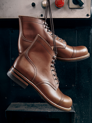 Brown leather boots with laces hanging on a dark surface