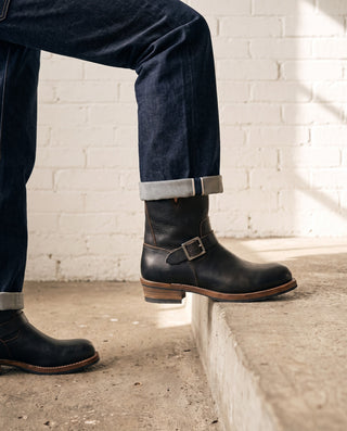 Black 3530 engineer boots with one foot up on a concrete ledge