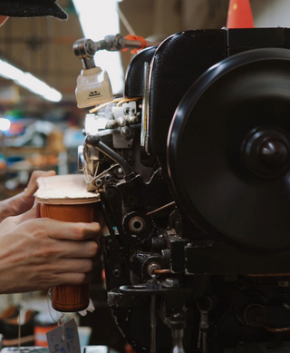 Person holding a boots near a large machine to make a goodyear welted boots