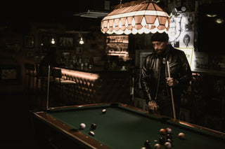 Wide dive bar interior with a rider in a leather jacket at the lit pool table