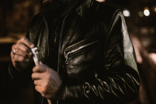 Close-up of a black leather jacket chest and zip pockets in low garage light