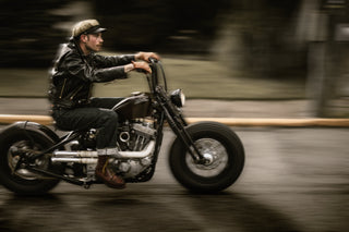 Panning shot of a rider on a bobber, black leather jacket and brown boots