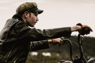 Profile of a rider in a cap and black leather jacket with brown leather gloves