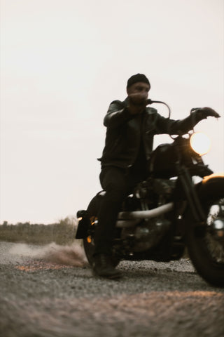 Rider pulling away on gravel at dusk, dust kicking off the rear tire