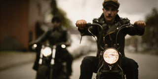 Two riders on bobbers rolling toward camera, front headlights lit, Brake House leather jackets